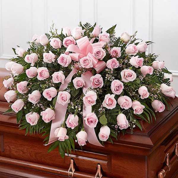 Pink rose casket spray with ribbon on a wooden casket