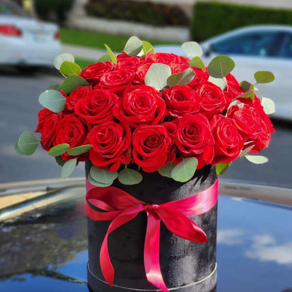 Red roses in a black hatbox with a pink ribbon