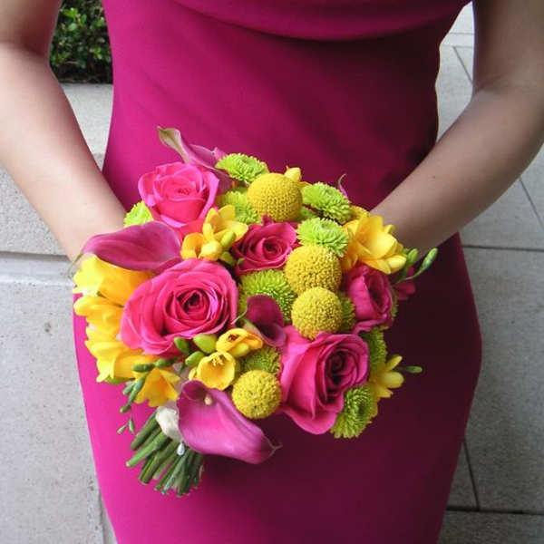 Woman holding a bright pink bouquet with roses, calla lilies, and yellow flowers
