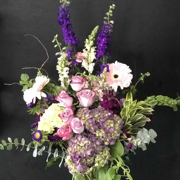Mixed bouquet with pink roses, hydrangeas, and tall purple blooms in a glass vase