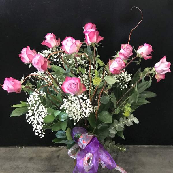 Pink roses arranged in a vase with baby's breath and ribbon