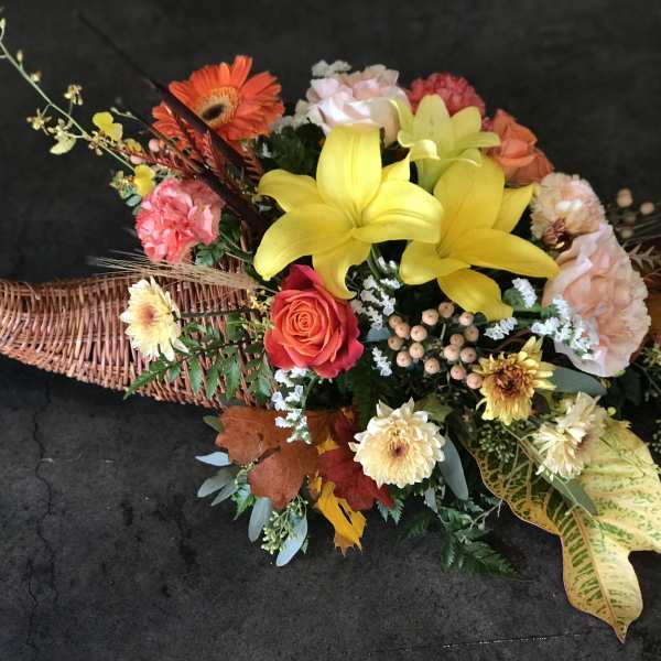 Colorful floral arrangement in a woven basket with yellow lilies and orange gerberas
