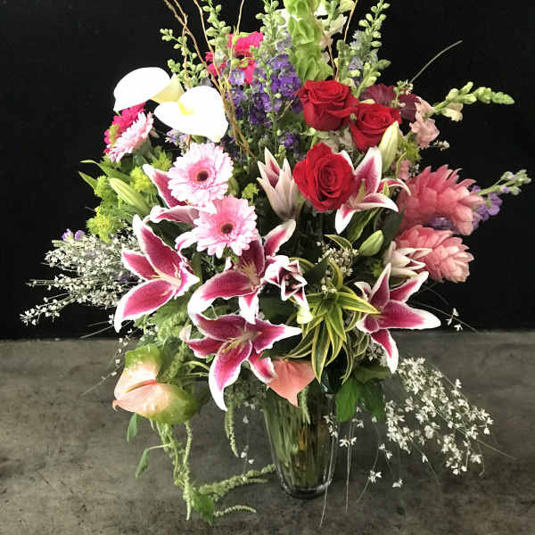 Large mixed bouquet with pink lilies, red roses, and white calla lilies in a glass vase