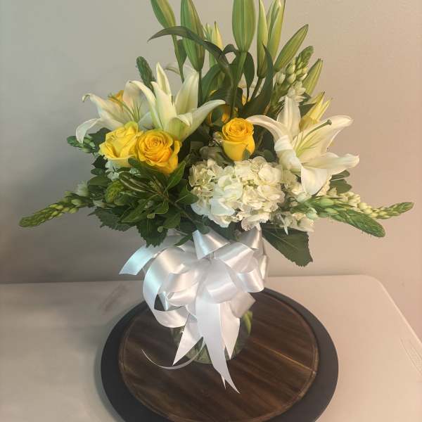 Bouquet of white lilies, yellow roses, and white hydrangeas in a glass vase with a white ribbon