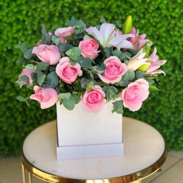Pink roses and white lilies arranged in a white box