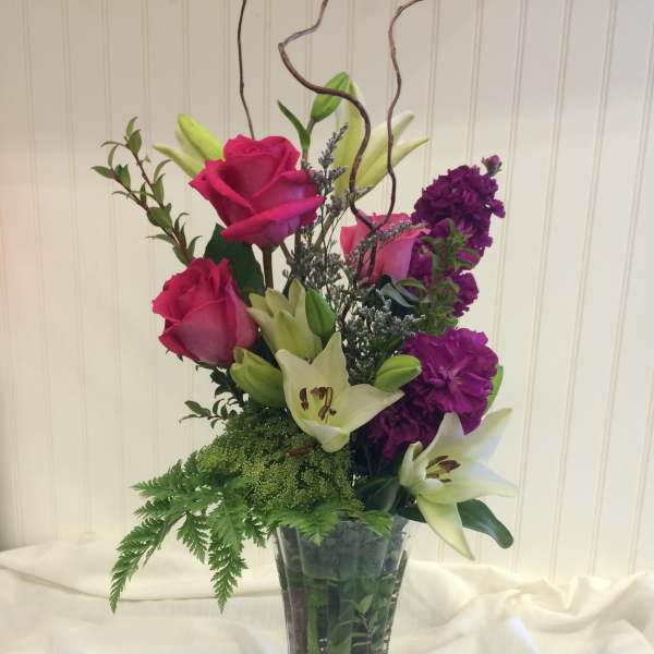 Tall bouquet of pink roses, white lilies, and purple flowers in a glass vase
