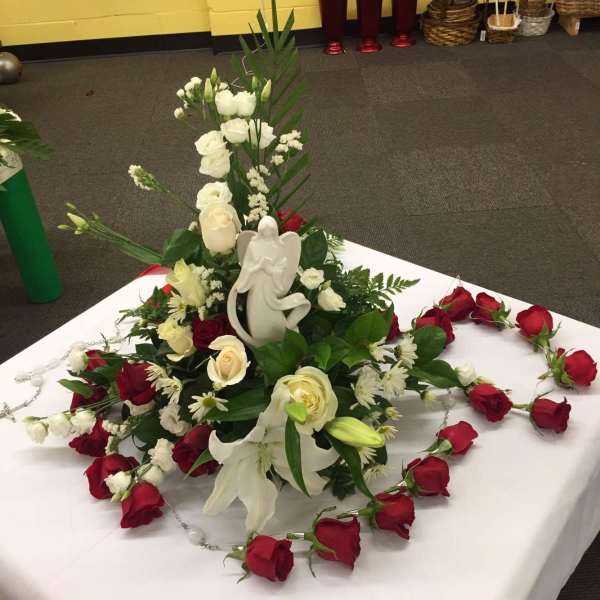 White rose and lily arrangement with an angel figurine and red rose garland