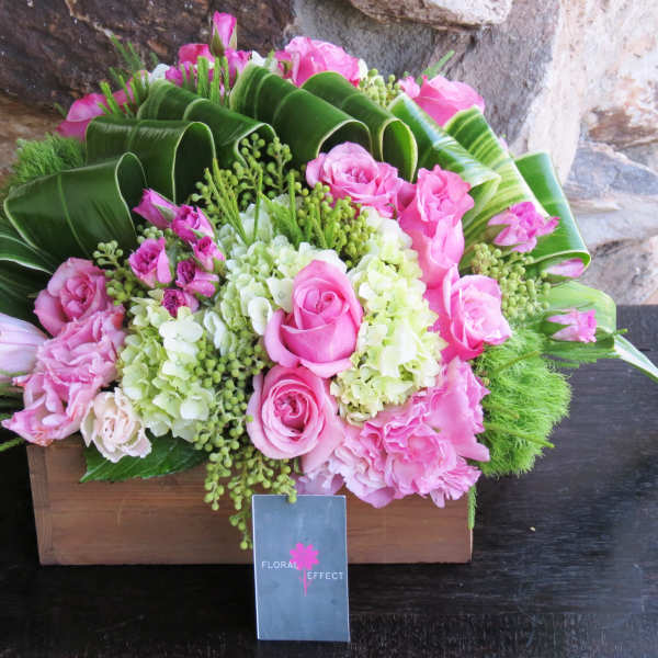 Pink roses and hydrangeas in a wooden box with large green leaves