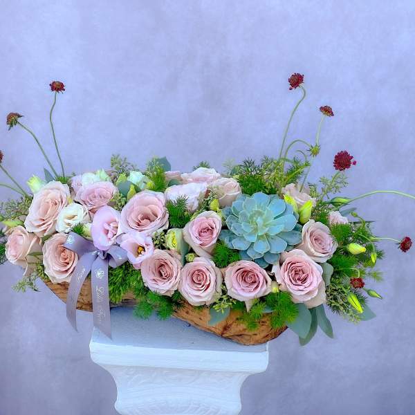 Low floral arrangement of pale pink roses and a blue succulent in a wooden container