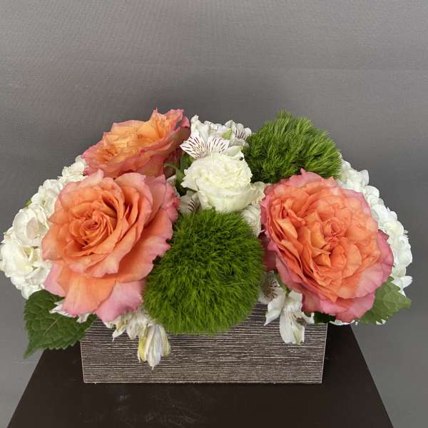 Orange roses and white flowers arranged in a rectangular box with green moss accents