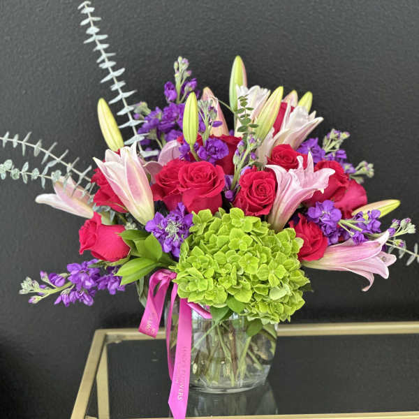 Bouquet of pink roses, lilies, and purple flowers in a glass vase