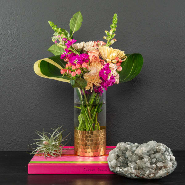 Mixed bouquet in a glass vase with bright pink flowers and large leaves