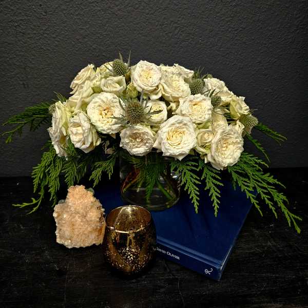Cream rose bouquet in a glass vase with green foliage and a candle