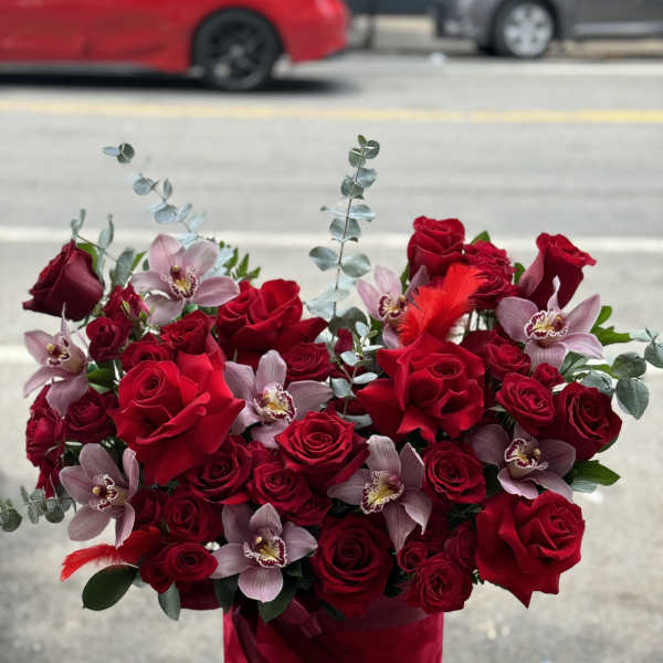 Red roses and pale orchids arranged in a red hat box