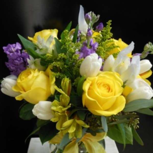 Yellow roses and white tulips in a glass vase with purple accents