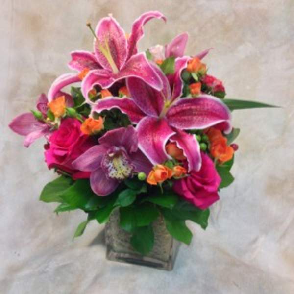 Pink lilies and roses arranged in a square glass vase