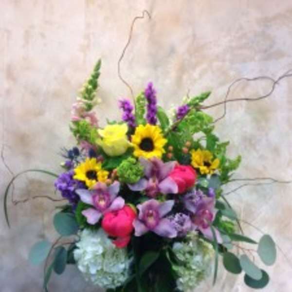 Mixed bouquet with sunflowers, purple orchids, and pink blooms in a glass vase