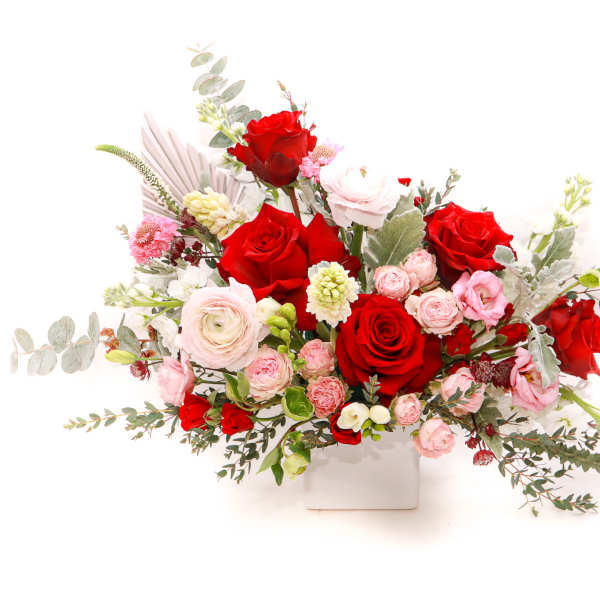 Red and pink rose arrangement in a white square vase