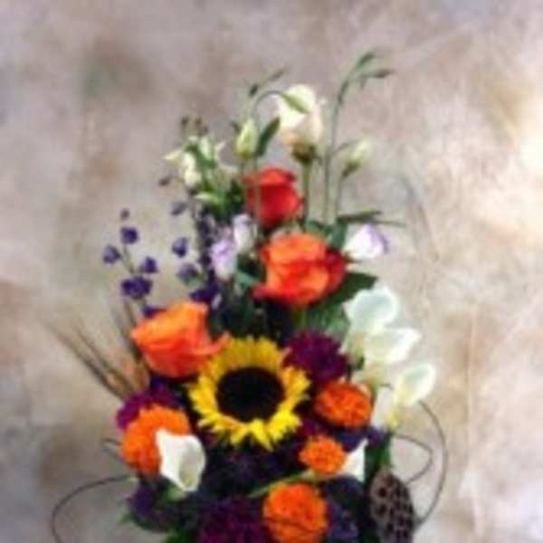 Tall colorful floral arrangement in a black vase with a sunflower and calla lilies