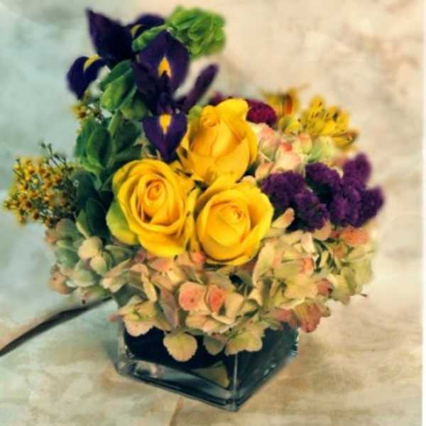 Yellow roses and purple irises in a square glass vase