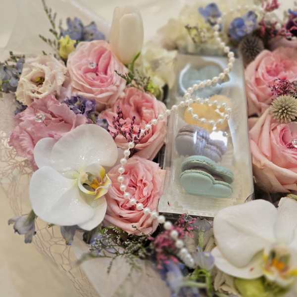 Pink roses and white orchids arranged around a clear box of macarons