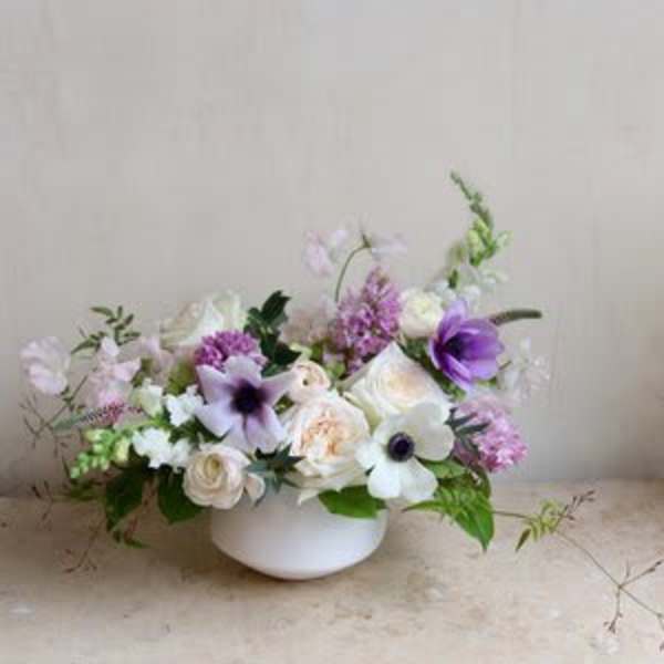 Low floral arrangement in a white bowl with white and purple blooms