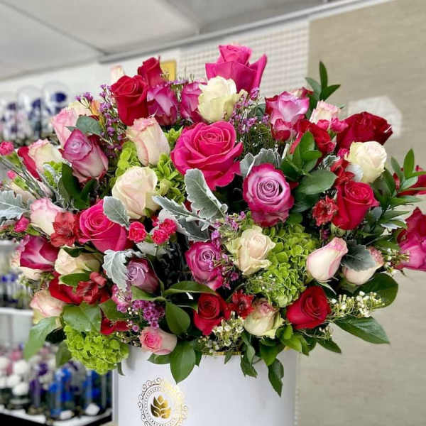 Large arrangement of red, pink, and ivory roses with green accent blooms in a white hatbox container