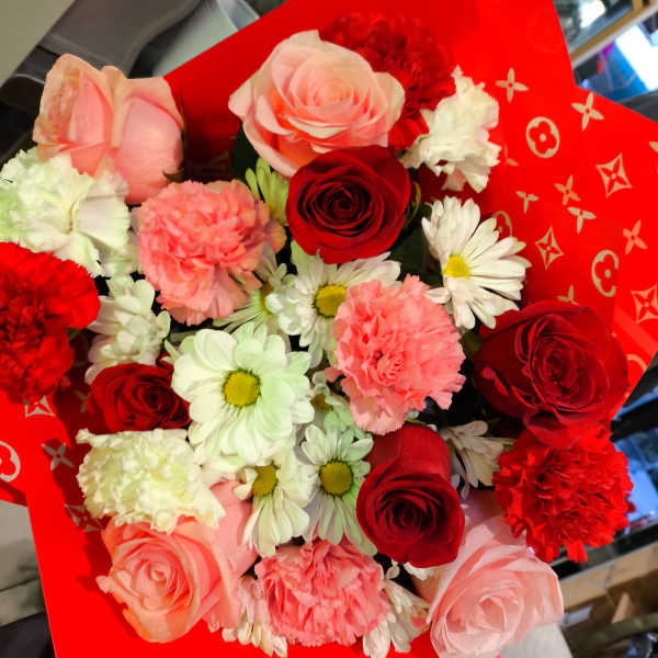 Bouquet of red and pink roses with white daisies and carnations in red wrap