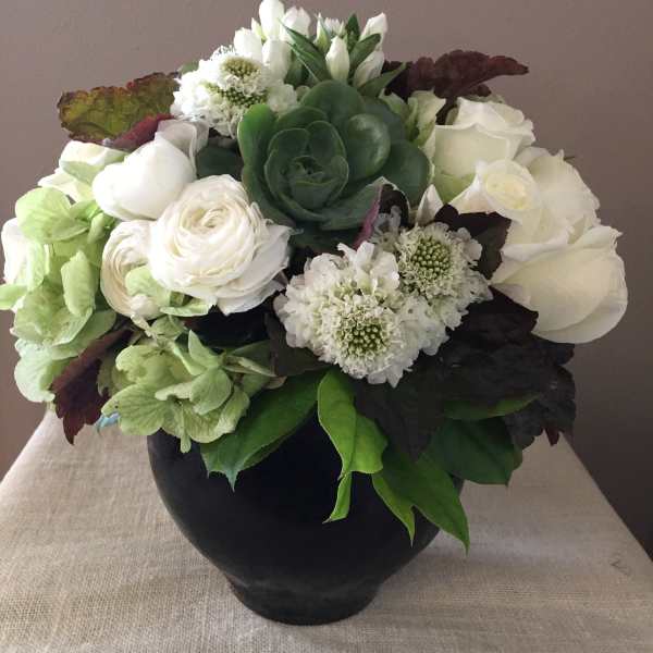 White floral arrangement in a black vase with a green succulent center