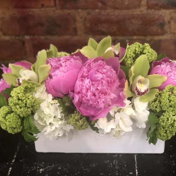 Pink peonies and green orchids in a white rectangular vase