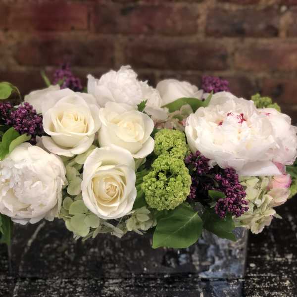 White roses and peonies with green and purple accents in a low arrangement