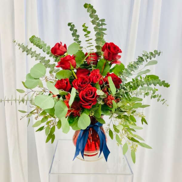 Red roses in a glass vase with blue ribbon and airy greenery