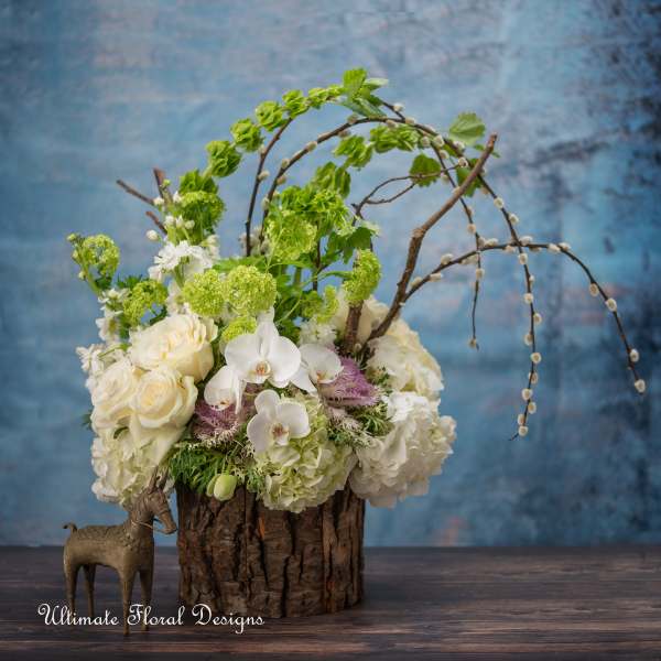 White and green floral arrangement in a rustic wood container with arched branches