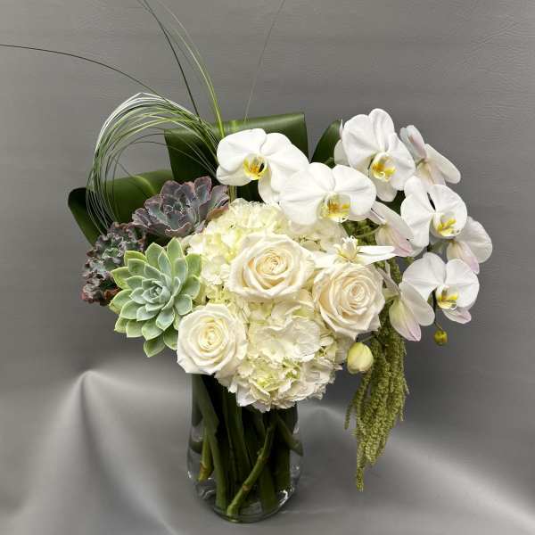 White orchids, roses, hydrangea, and succulents in a clear glass vase