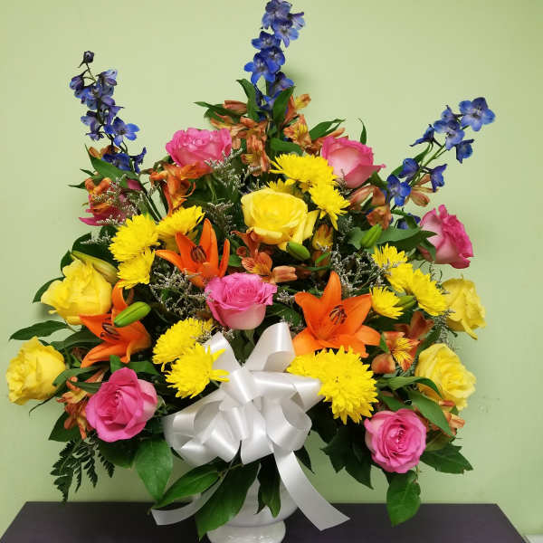 Colorful mixed flower arrangement in a white vase with a white bow