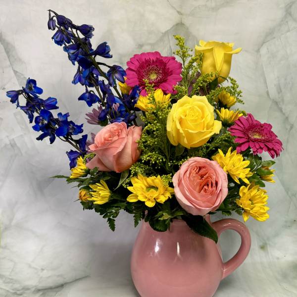 Mixed bouquet of pink, yellow, and blue flowers in a pink pitcher vase
