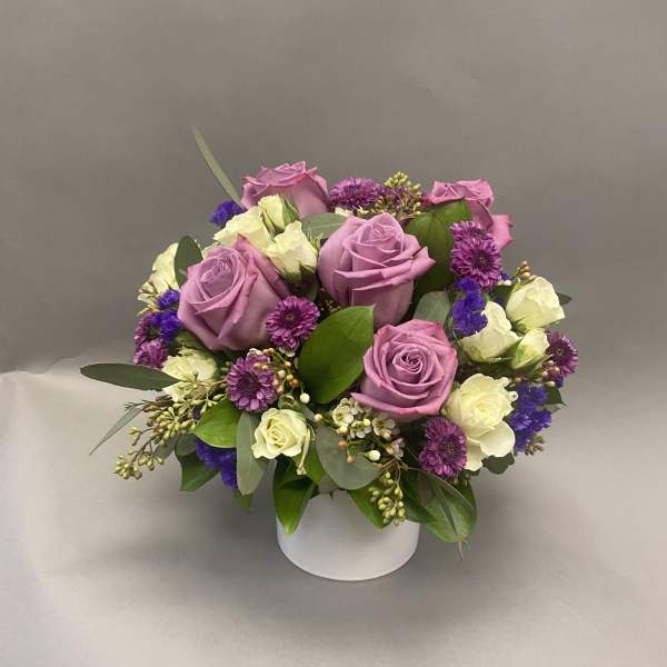 Lavender roses and purple flowers arranged in a white vase