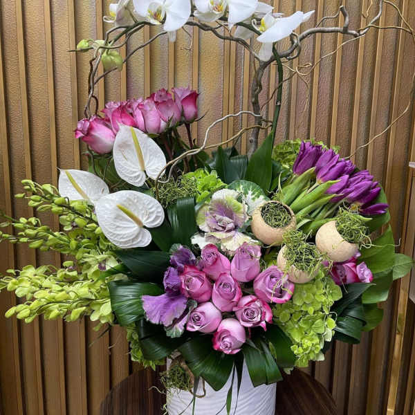 Pink and white floral arrangement in a white vase with orchids and roses