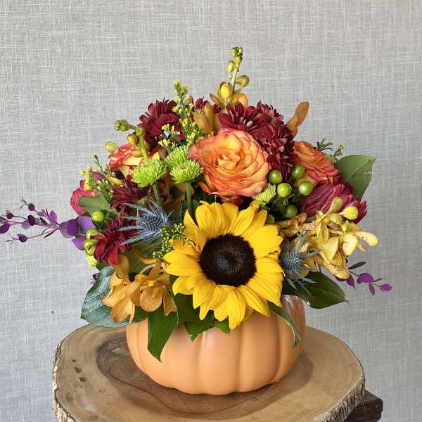 Mixed bouquet in a pumpkin-shaped vase with a sunflower and orange roses