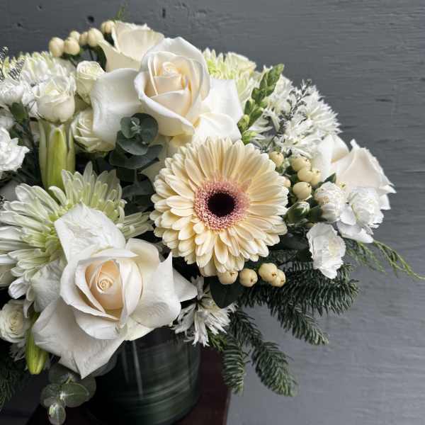 White roses and a pale peach gerbera daisy in a dark vase