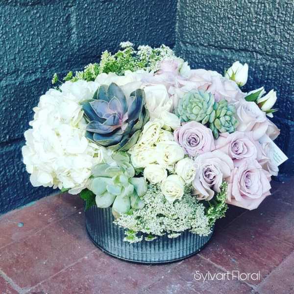 Round floral arrangement with pale roses, hydrangeas, and succulents in a black container