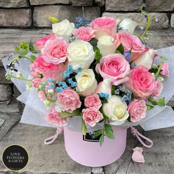 Pink and white rose arrangement in a round pink hatbox with blue filler flowers