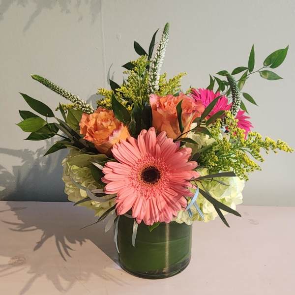 Pink gerbera bouquet in a green vase with peach roses and white hydrangeas