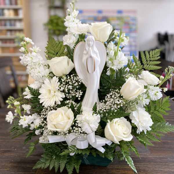 White roses and daisies arranged around a praying angel figurine
