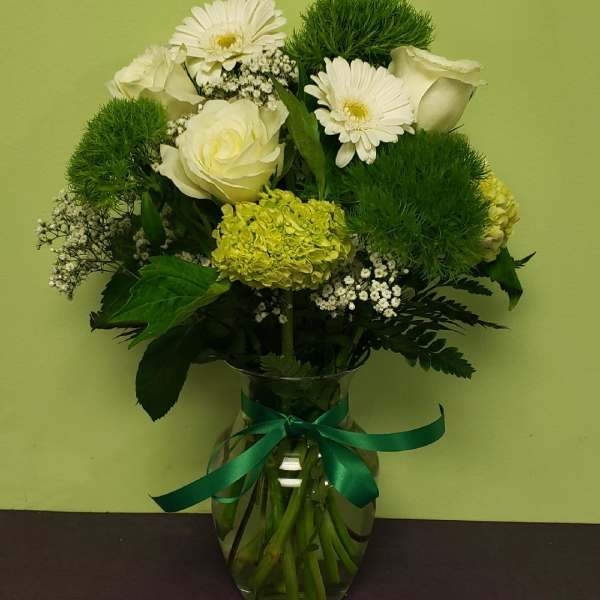White flowers and green blooms arranged in a glass vase with a ribbon