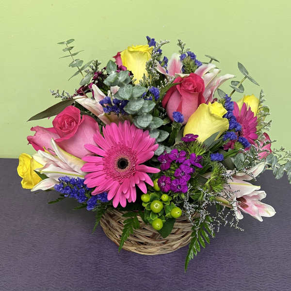 Basket arrangement with pink roses, gerbera daisies, lilies, and purple filler flowers