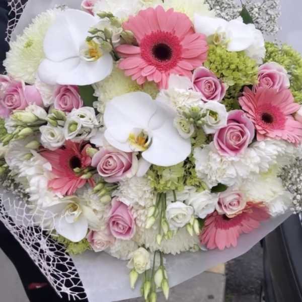 Handheld bouquet of pink gerberas, white orchids, and roses wrapped in white paper