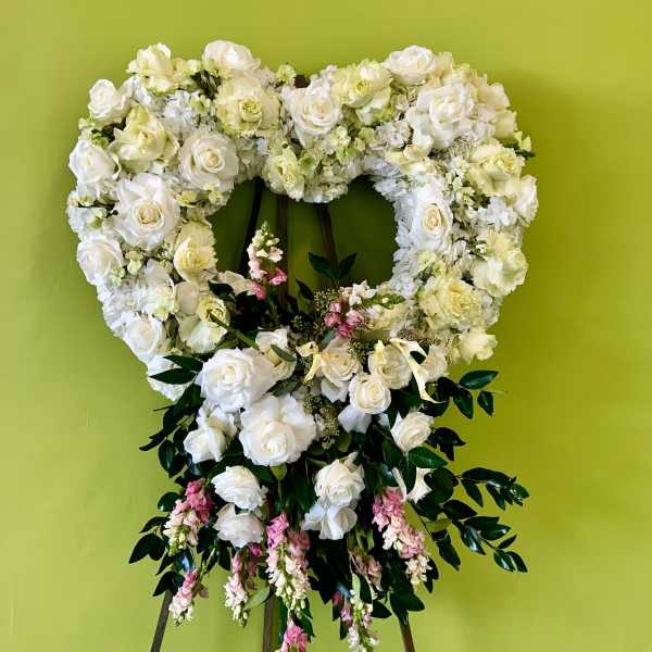 Heart-shaped white floral wreath on an easel with pink accents