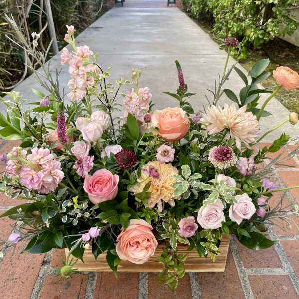 Low floral arrangement with pink, peach, and lavender blooms in a wooden container