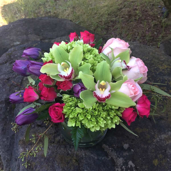 Bouquet of pink roses, purple tulips, and green orchids in a glass vase